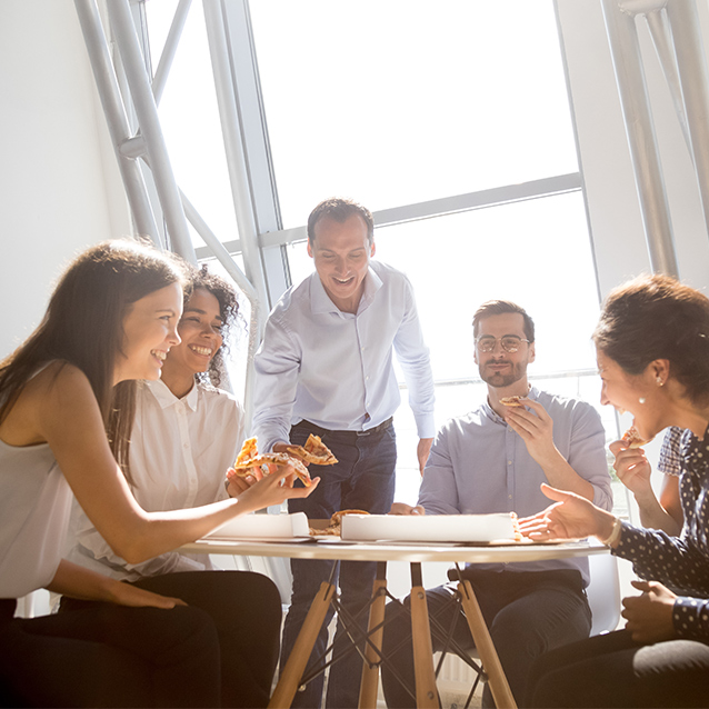 Cheerful diverse team of workers laughing at funny joke while eating a corporate lunch in office room