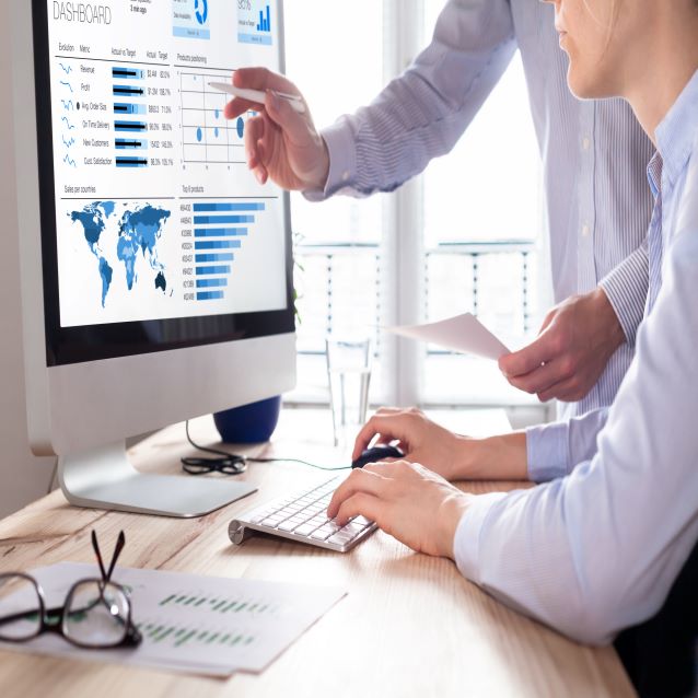 Meeting at a desk and talking about web analytic data displayed on a computer monitor.